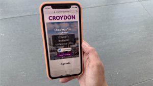 A hand holding a phone, viewing the mobile version of the Croydon Leaders website. It shows the title "Shaping our Future", a link to twitter with the hashtag #croydonleaders, a link to the feedback survey and the agenda at the bottom.